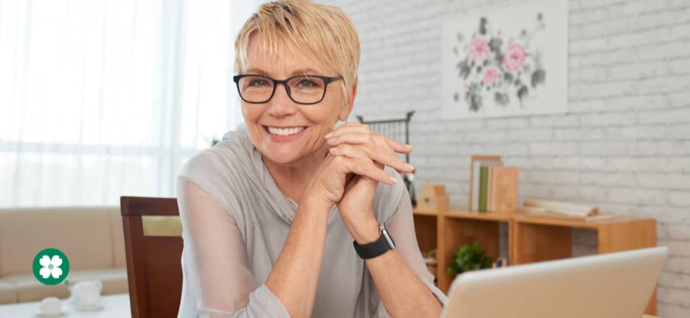 Retirement age woman sitting at a table smiling with a laptop