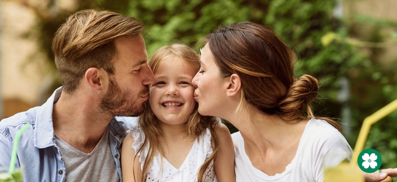 parents kissing child on both sides of her face